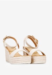 Sandales compensées avec un dessus en crème tissé, une bride de cheville et une semelle intérieure lisse en tan. Présente une plateforme en jute tressé texturé.