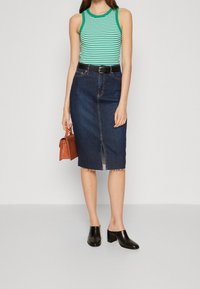 Falda lápiz de mezclilla con dobladillo deshilachado y abertura central, combinada con una camiseta de tirantes a rayas verde y blanca. Mules de tacón bloque negro y bolso marrón.