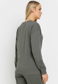 Sudadera gris de corte relajado, con cuello redondo y puños de canalé. Fabricada con una tela suave y de textura lisa.