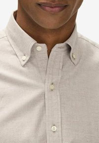 Ljusbeige skjorta med knappar och klassisk krage, med en strukturerad yta och små, runda, pärlemorliknande knappar.