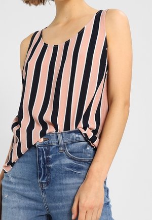 Woman wearing sleeveless tank top with vertical pink, black, and white stripes tucked into blue denim jeans.