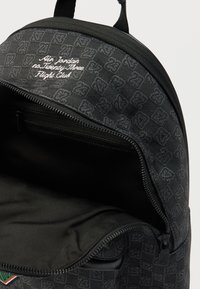 Black backpack with a zippered opening, featuring a subtle checkered pattern and white embroidered text. Soft interior lining, durable material.