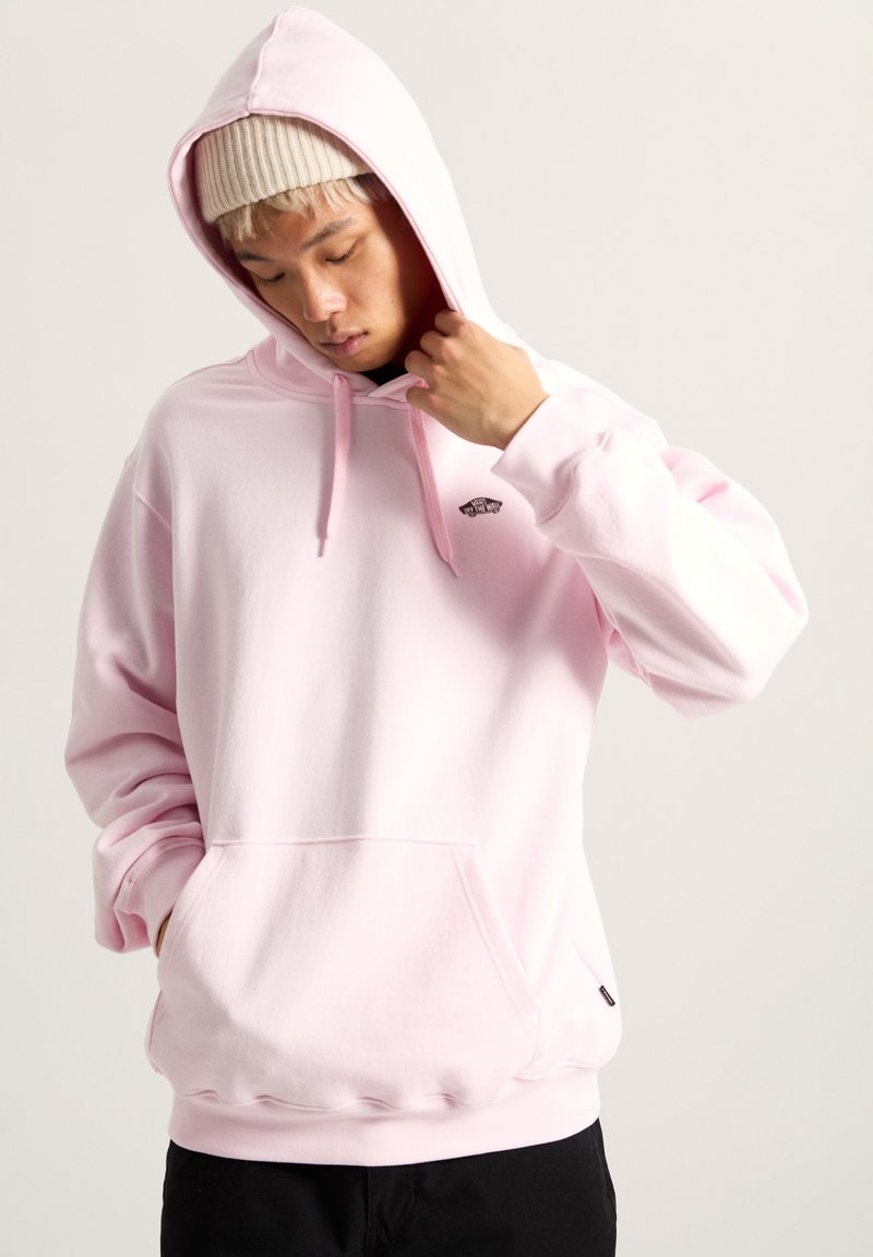 Rosa Kapuzenpullover mit einer Fronttasche, Kordelzügen und einem kleinen schwarzen Logo auf der linken Brust. Weicher Stoff, lockere Passform und gerippte Bündchen.