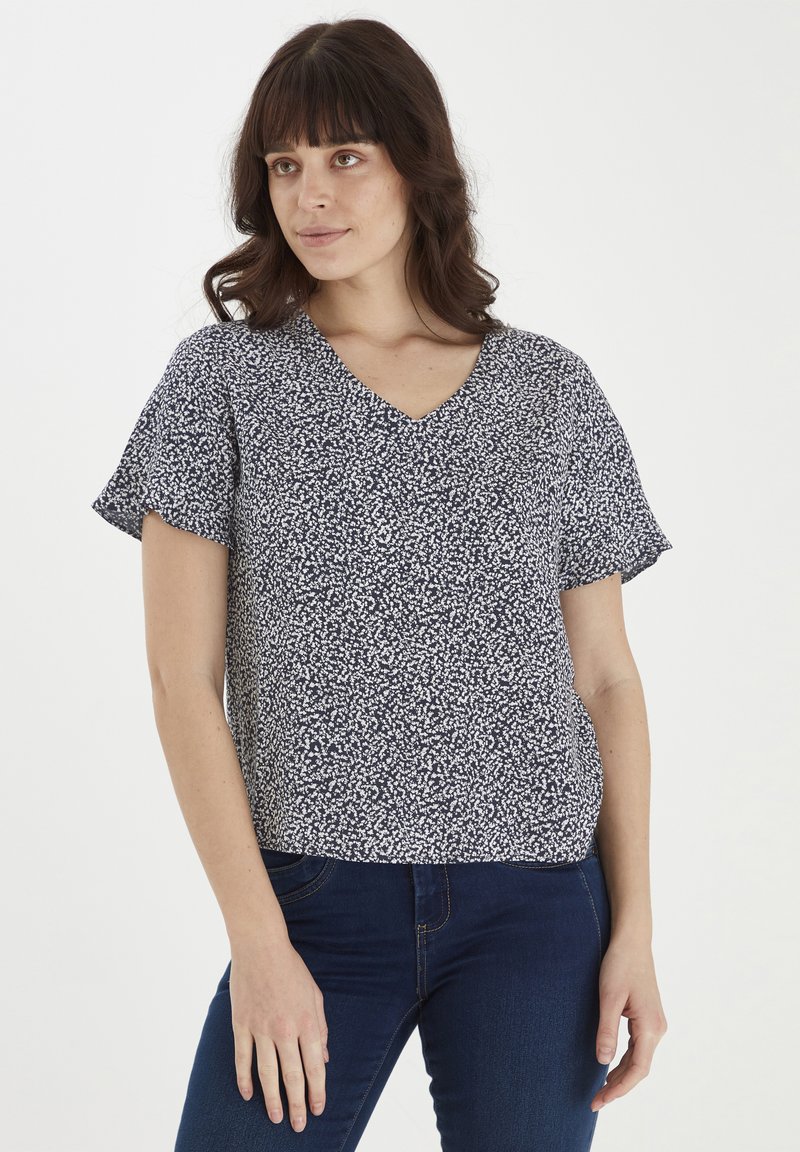 Blusa a righe navy con scollo a V, maniche corte a sbuffo e vestibilità comoda. Il tessuto presenta un piccolo motivo a macchie bianche.