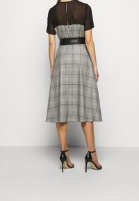 Une robe midi avec un haut transparent noir et une jupe grise à carreaux dotée d'une taille ceinturée. Le tissu a une texture lisse et l'ourlet s'évase doucement.