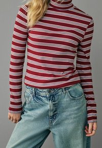 Haut à col roulé à manches longues rayé bordeaux et blanc, associé à un jean en denim bleu clair taille haute. Tissu texturé, coupe décontractée.