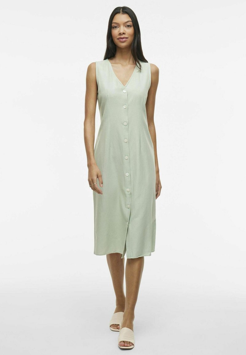 Robe sans manches vert clair avec décolleté en V et fermeture à boutons sur le devant, fabriquée dans un tissu doux. Longueur genoux avec une coupe droite et une texture subtile.