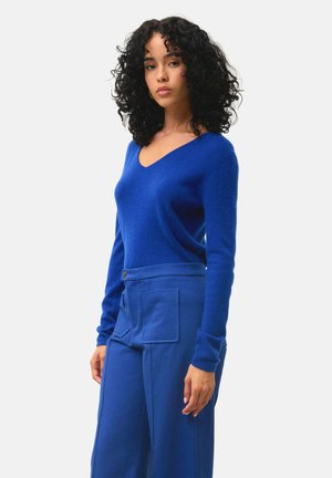 Maglione azzurro in lana a V con maniche lunghe abbinato a pantaloni azzurri a vita alta con tasche laterali e dettaglio con bottoni.