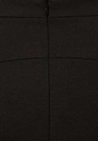 Jupe moulante noire avec une texture lisse, une fermeture éclair au dos et des détails de coutures horizontales.