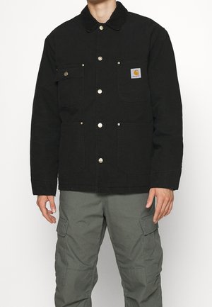 Sort lærredjakke med trykknapper, to brystlommer og cord-fløjlskrave. Båret over grå cargo-bukser for et praktisk look.