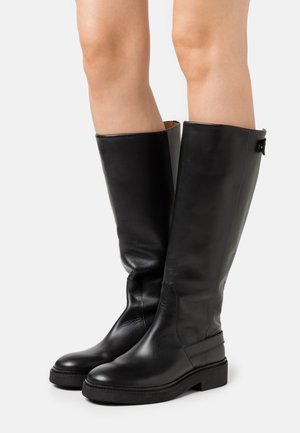 Černé kožené vysoké boty po kolena s hladkým povrchem, kulatou špičkou, plochou podrážkou a malým dekorativním kovovým akcentem vzadu.