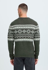 Pulover tricotat verde cu un design patternat în gri deschis, având fulgi de nea și forme geometrice pe piept și mâneci.