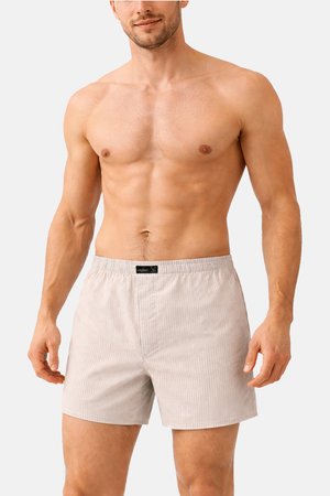 Hemdloser Mann, der hellbeige gestreifte Boxershorts trägt, steht vor einem schlichten weißen Hintergrund.