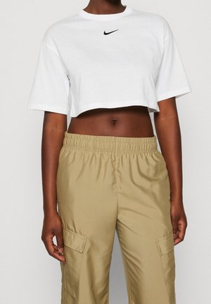 Personne portant un t-shirt Nike blanc court et un pantalon cargo beige à taille élastique, debout devant un fond clair uni.