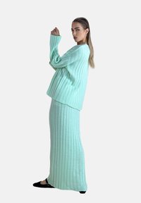 Mintgrøn ribstrikket sweater og matchende nederdel med lange ærmer og løs pasform. Glat tekstur med lodrette linjer.