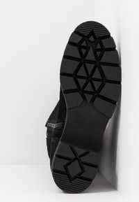 Czarne buty sportowe sięgające do kostki z teksturowaną gumową podeszwą, posiadającą geometryczny wzór bieżnika. Cholewka wykonana z miękkiego zamszu, w tym z detalami zamka błyskawicznego.