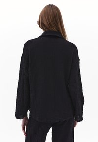Giacca nera a texture con vestibilità rilassata, dotata di colletto a punta e maniche lunghe. Abbinata senza soluzione di continuità a pantaloni in tessuto simile.