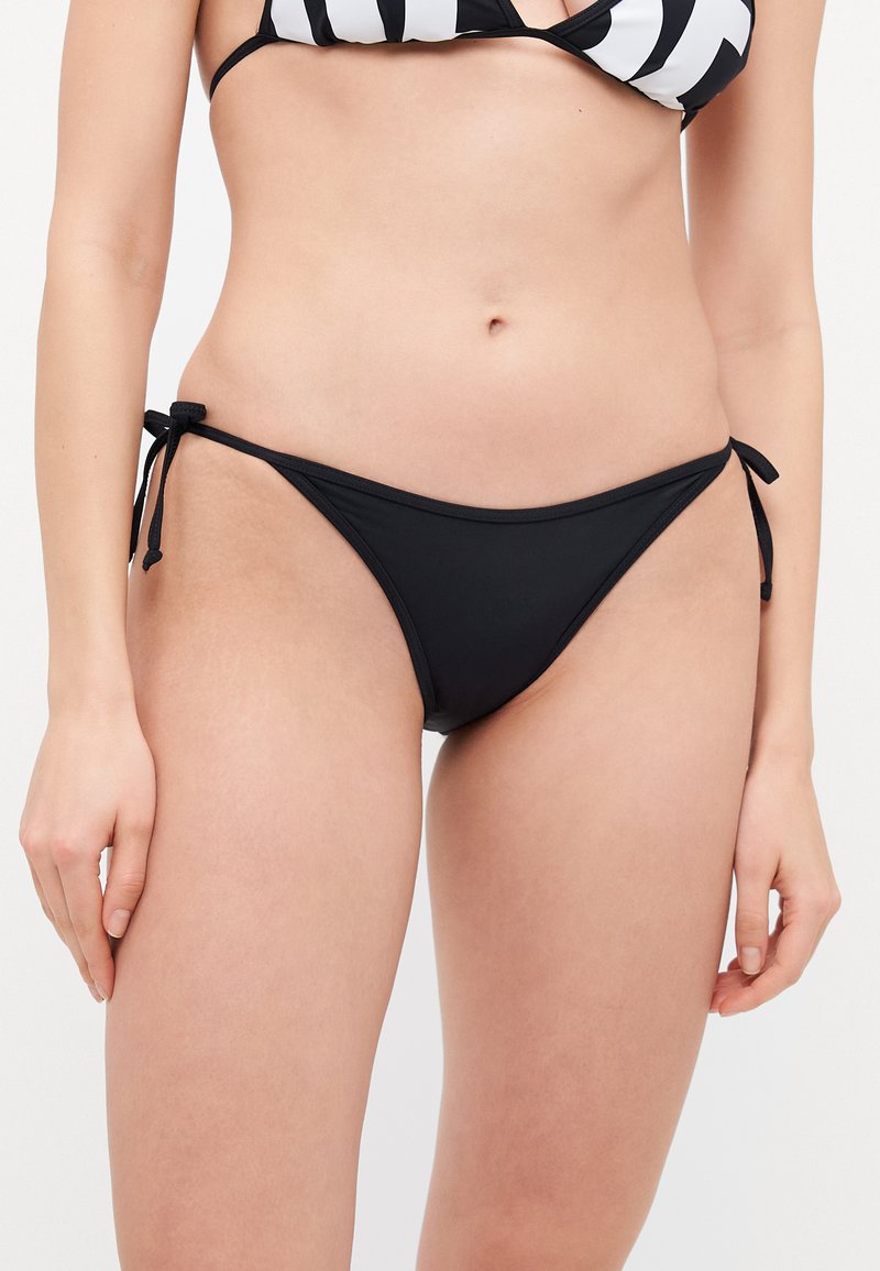 Fekete bikini alsó állítható oldalszíjakkal, sima anyagból készült, klasszikus kialakítással. Minimalista szab�ás, amely jól kombinálható fürdőfelsőkkel.
