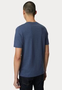 Modré tričko s krátkým rukávem, kulatým výstřihem a měkkou, hladkou texturou. Pohled z zad zobrazuje jednobarevný design bez vzorů nebo jakýchkoli dekorací.