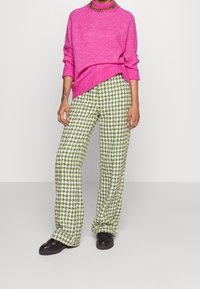 Rosa stickad tröja med hög krage, kombinerad med gröna och vita hundtandsmönstrade byxor med vida ben. Svarta klumpiga stövlar.