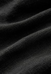 Gros plan sur un tissu noir froissé montrant une texture tissée détaillée et des reflets lumineux subtils.