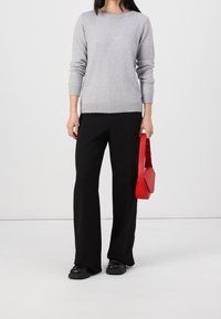Gray knit sweater with a round neckline, ribbed cuffs, and hem, paired with black wide-leg trousers. Carrying a red leather handbag.
