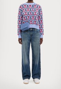 Suéter de punto azul claro con estampado floral rojo, combinado con jeans holgados de mezclilla azul y zapatillas blancas. Pequeño bolso cruzado azul.