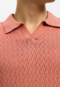 Strikket polo skjorte i støvet rosa, med et teksturert mønster med diamantformer, en klassisk krage og V-halsdesign.