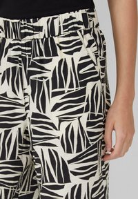 Pantalons à motifs noir et blanc avec une taille élastique et des poches, ornés de motifs de feuilles abstraites et audacieuses sur un tissu texturé.