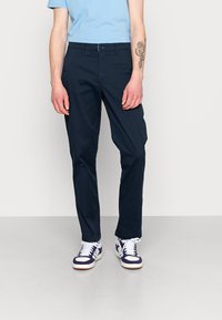Marineblaue Chinos aus Baumwolle mit geradem Bein, vorderen Taschen und Knopfverschluss, kombiniert mit weißen und lila Sneakern.
