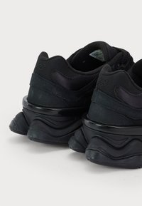 Baskets noires en matériaux mesh et cuir, avec une semelle épaisse et un design ondulé distinctif en textures variées.
