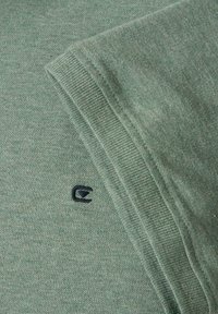 Zielony sweter wykonany z miękkiego, teksturowanego materiału, z okrągłym dekoltem i małym, ciemnym logo wyszytym na klatce piersiowej.