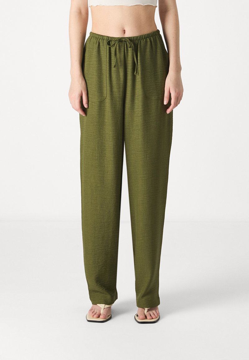 Pantaloni ușori de culoare verde măsliniu, cu talie elastică, buzunare laterale și o croială lejeră, asortați cu un top alb scurt.