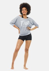 Light gray oversized shirt with white text "First I need coffee," paired with black shorts. The fabric appears soft and casual.