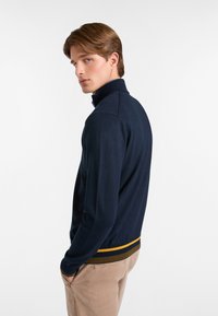 Dunkelblauer Pullover mit hohem Kragen, gerippten Bündchen und einem Saum mit gelben und braunen Streifen. Weicher Stoff mit figurbetontem Design.