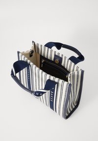 Sac fourre-tout en toile rayée bleu marine et blanc. Comprend deux anses, une poche zippée et une forme carrée au design non structuré.