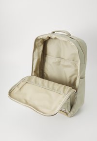 Beige backpack with a zippered opening, showing a spacious interior and a padded compartment. Smooth outer material and textured inner lining.