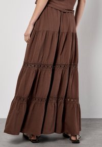Gonna maxi marrone con design a strati, dettagli in pizzo e tessuto leggero. Orlo a campana visibile e vestibilità comoda.