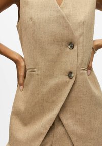 Beige hørflet vest med dyb V-hals, to knapper og sidelommer. Har skræddersyet pasform og subtil tekstureret stof.