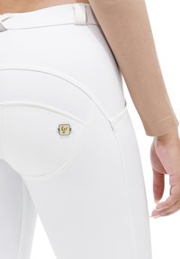 Leggings blancs taille haute avec des coutures, coupe slim et un petit logo carré sur la poche arrière, présentant une texture mate lisse.