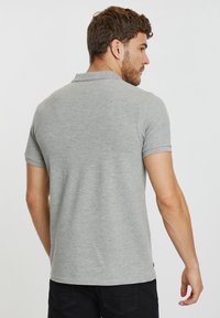 Camisa polo de manga corta gris con cuello clásico y dobladillo recto, que presenta una sutil textura y sin patrones o acentos visibles.