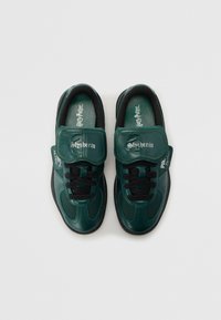 Zapatillas deportivas verdes con un diseño texturizado, con cordones negros y una correa de velcro. Logos de "Slytherin" y "Harry Potter" en la lengüeta y la plantilla.