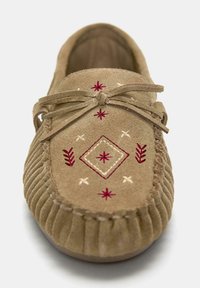 Mocassino in suede marrone con pattern geometrici ricamati in rosso e bianco e un fiocco legato sulla parte superiore.