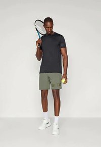 Must have lühikeste varrukatega sportlik särk, oliivrohelised lühikesed püksid, millel on trükitud "BORG", valged jooksujalanõud, hoides tennisepalli ja reketit.