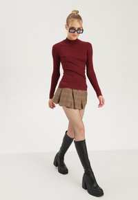 Hladký burgundský top s dlouhým rukávem, kostkovaná hnědá skládací mini sukně, punčocháče s rybími síťkami a černé kozačky na vysokém podpatku až ke kolenům. Noseny jednoduše sluneční brýle.