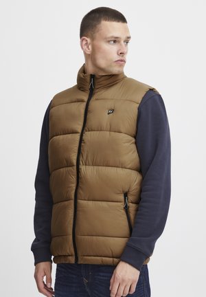 Bruine puffer bodywarmer met hoge kraag, ritssluiting aan de voorkant en zijzakken. Draagt over een marineblauw overhemd met lange mouwen, dat voorzien is van doorgestikte secties.