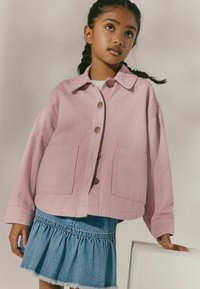 Veste rayée rose avec de grands boutons et deux poches avant, associée à une jupe en denim bleu avec un ourlet en volants. Texture lisse.