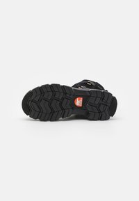 Black outdoor boot with a rugged rubber sole, deep treads for traction, and metal hardware accents. Designed for stability and durability.
