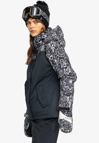 Snowboardjacke mit einem dunkelblauen Körper und gemusterten schwarz-weißen Ärmeln, ausgestattet mit Seitentaschen, einer Kapuze mit Kordelzug und weißen Handschuhen.