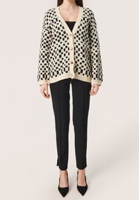 Svart och krämfärgad rutig cardigan med V-hals, stora knappar och ribbade ärmmuddar, ihopparad med svarta, slim-fit byxor och klackar.